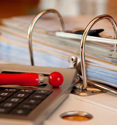 Ein offener Aktenordner mit einem Taschenrechner und einem roten Kugelschreiber auf einem Tisch.